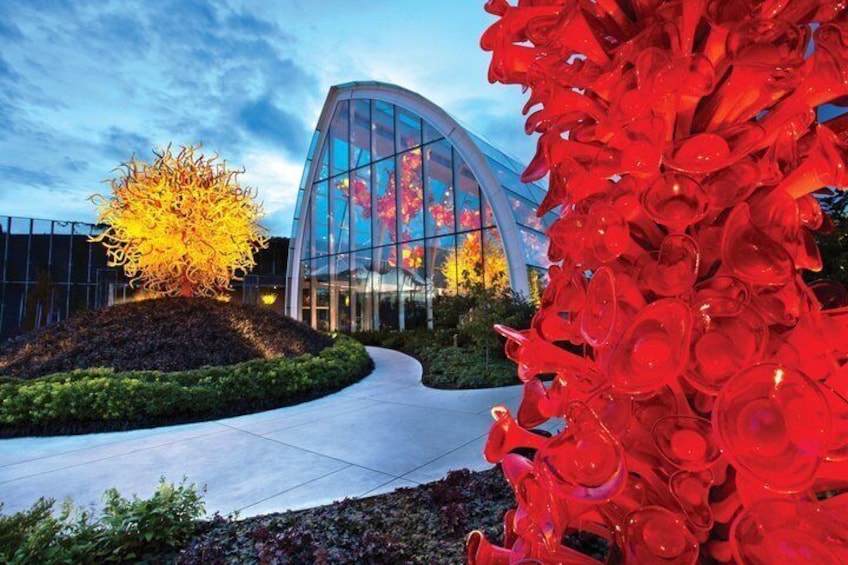 A modern building with a curved glass facade, a landscaped area with a tree, and a large red sculpture. 4