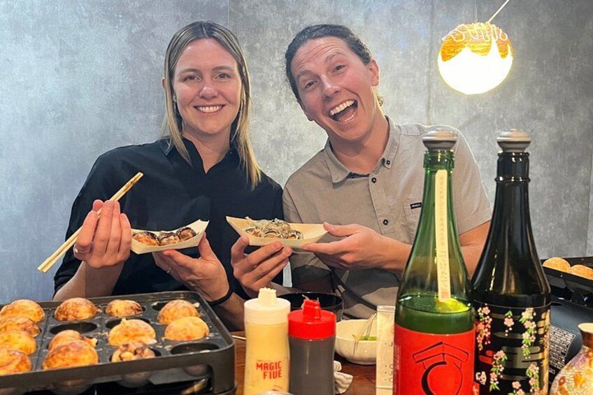 Dos personas sosteniendo comida, una parrilla con alimentos y botellas. 1