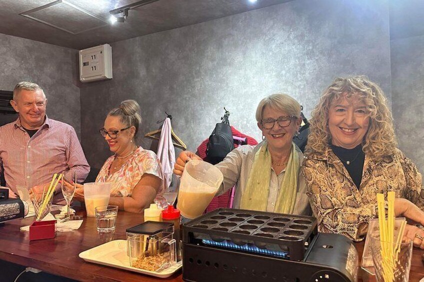 Un grupo de personas asistiendo a una demostración de cocina, con una máquina para gofres e ingredientes sobre la encimera. 5