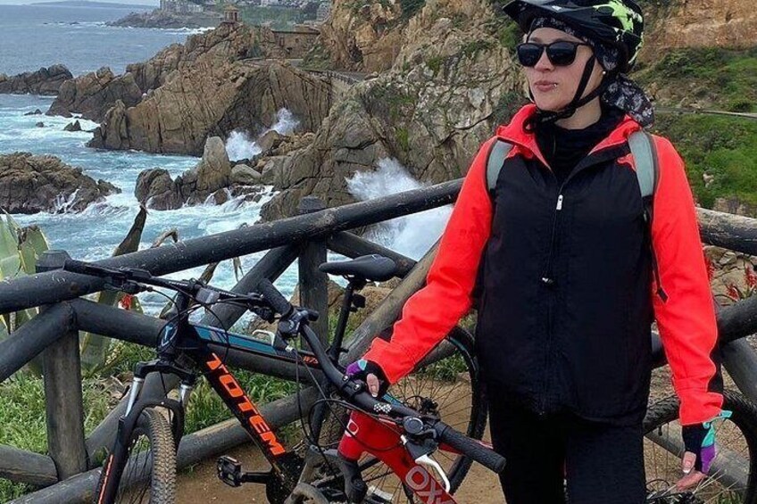 Una persona in piedi accanto a una mountain bike, con uno sfondo costiero roccioso. 2