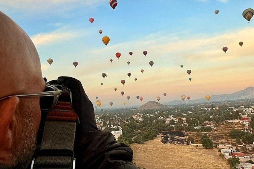 Una persona con el rostro desenfocado, un paisaje con edificios y numerosos globos aerostáticos en el cielo. 2