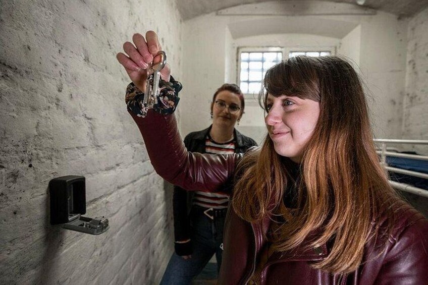 Una persona sostiene una llave en una habitación tenuemente iluminada, con una pared de ladrillo y una ventana. 3