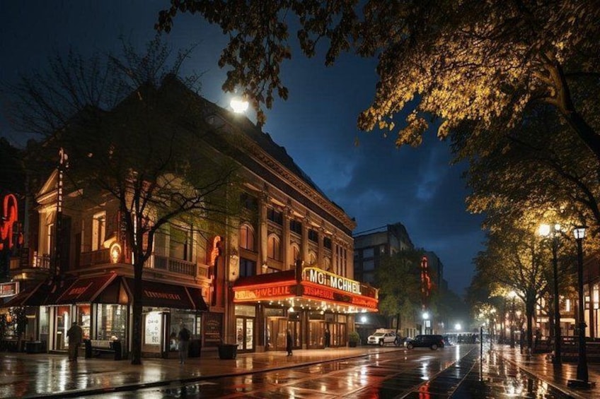Un théâtre historique, avec son auvent illuminé, et une rue mouillée qui reflète les lumières. 3