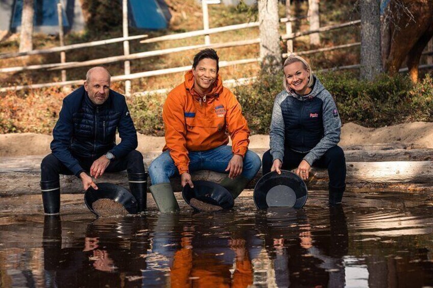 Three people sitting by a water body, holding black pans. 5