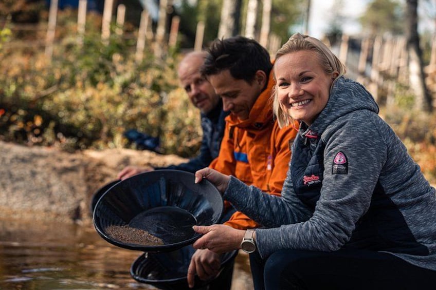 Two people sitting by a river, one holding a pan with fish. 1