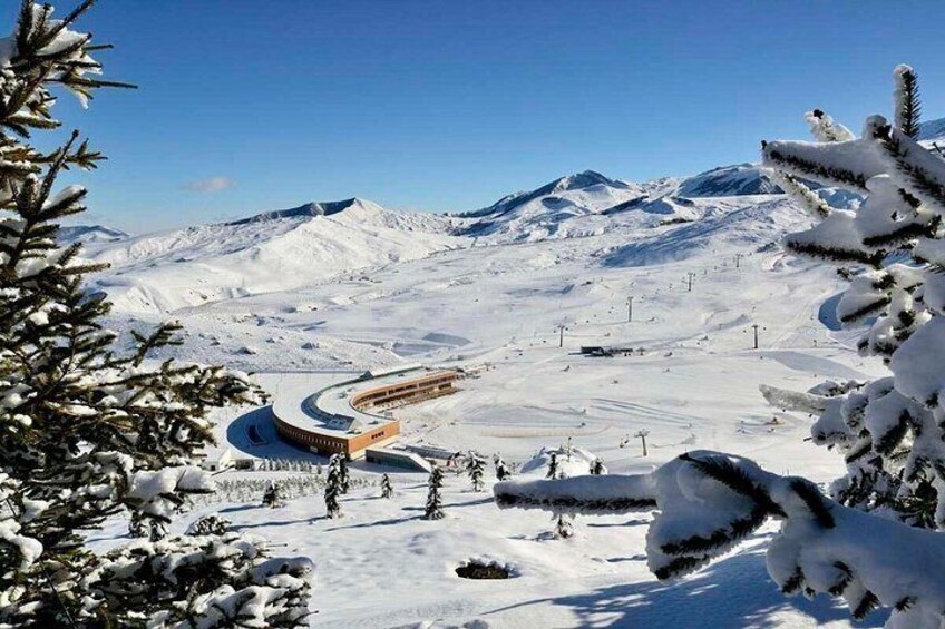 A snow-covered mountain landscape with a ski resort, including a curved building and ski lifts. 2