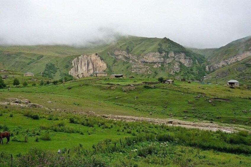 A mountainous landscape with green fields, a rocky outcrop, and a few small buildings. 5
