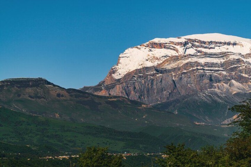 A snow-capped mountain with layered rock formations and a valley below. 4