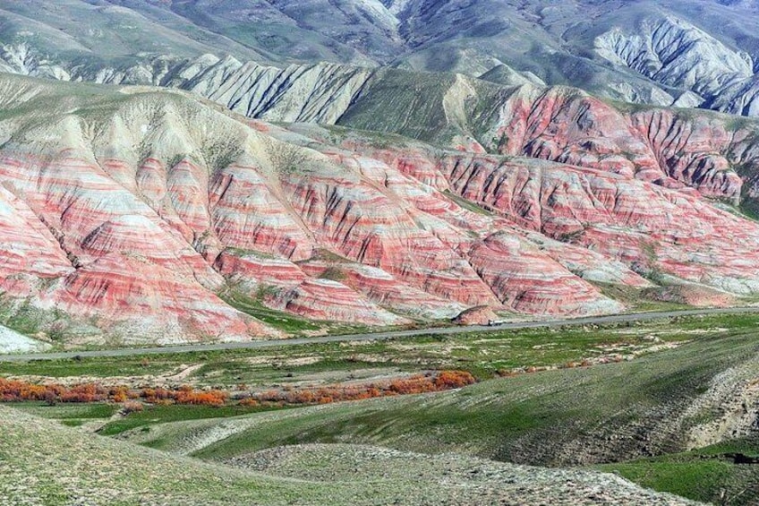 A landscape with layered rock formations in shades of pink and white, a road, and a distant mountain range. 1