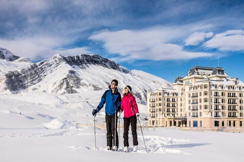 A snowy landscape with a large building and two people skiing. 2