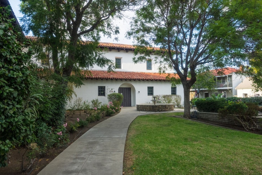 A white building with a red-tiled roof, surrounded by lush greenery and a well-maintained lawn. 5