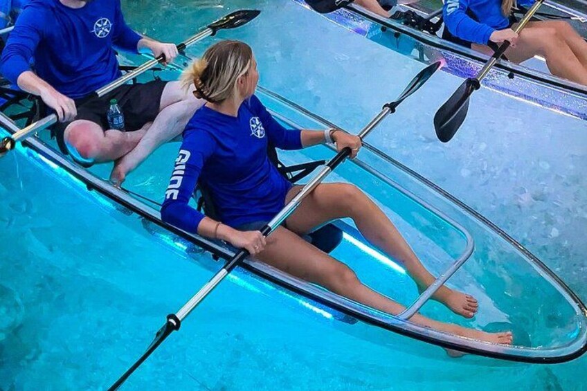 A person in a blue kayak with a paddle, wearing a blue shirt with white text, on a blue pool. 2