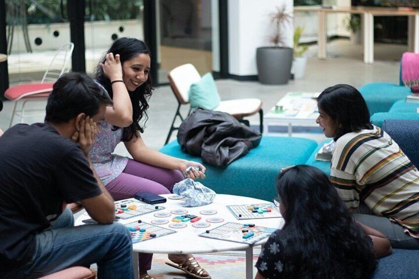A group of people sitting around a table playing a board game in a modern indoor setting with comfortable seating and a casual atmosphere. 3