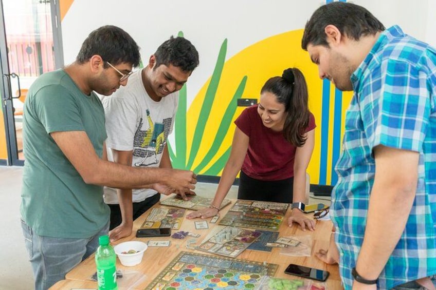 Eine Gruppe von Menschen spielt ein Gesellschaftsspiel am Tisch, mit Spielkarten und einem Mobiltelefon. 3