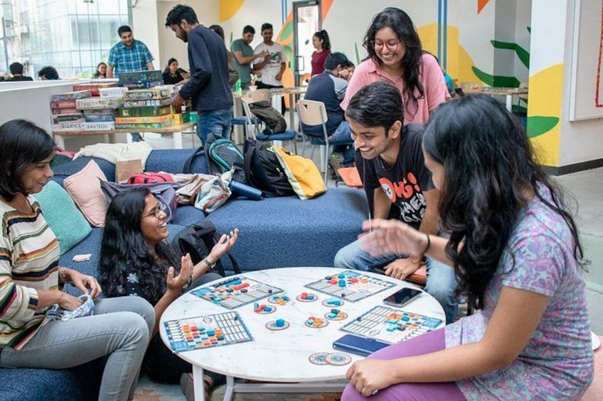 A group of people playing a board game in a casual indoor setting with colorful walls and a blue couch. 1