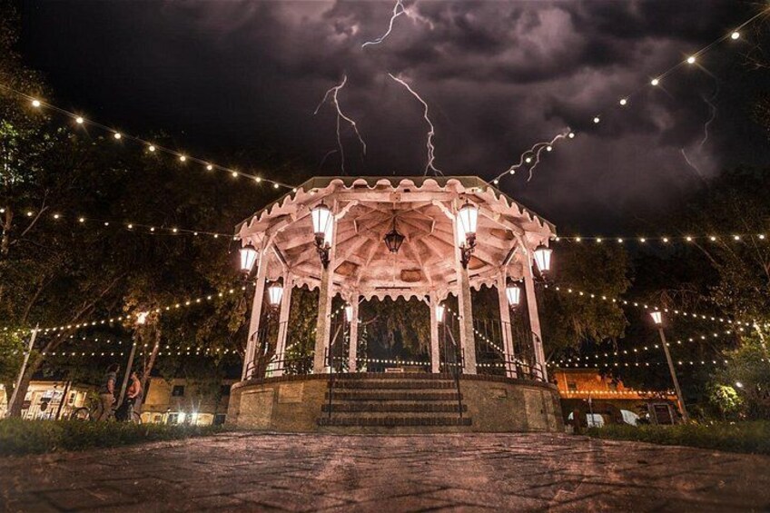 Un kiosque illuminé de guirlandes lumineuses, entouré d’arbres et surplombé par un ciel nuageux. 5