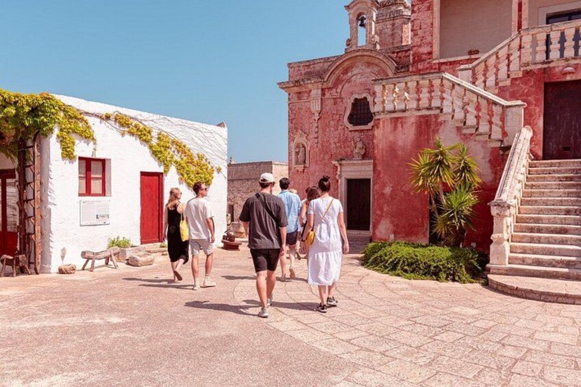 A group of people walking in a historic town square with buildings featuring red and white facades and a bell tower. 4