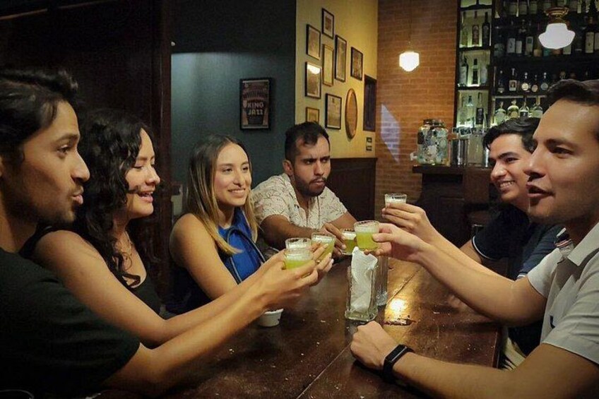 En grupp människor sitter vid ett bord på en bar och håller i varsin drink. 3