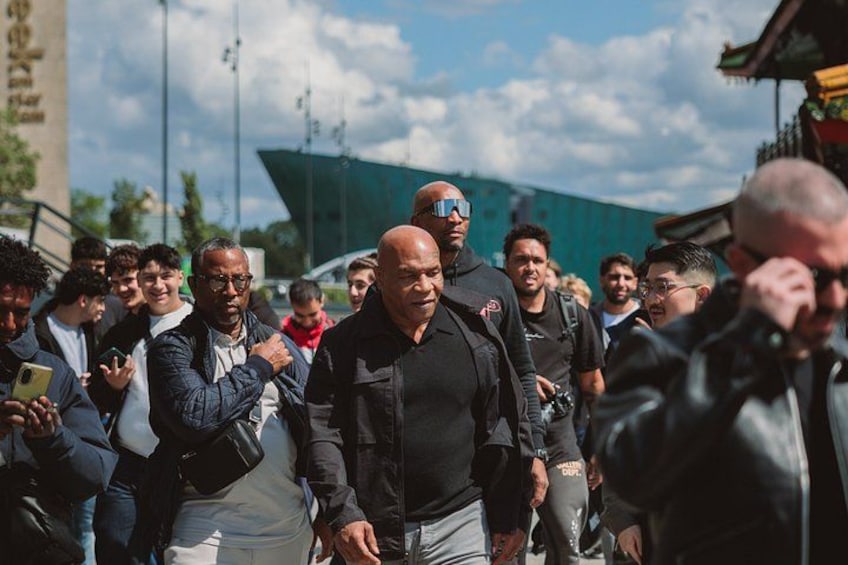 A group of people walking outdoors, some with cameras, in a sunny urban setting with buildings and a clear sky. 4