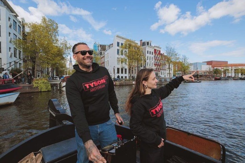 Two people on a boat in a canal with buildings in the background. 3