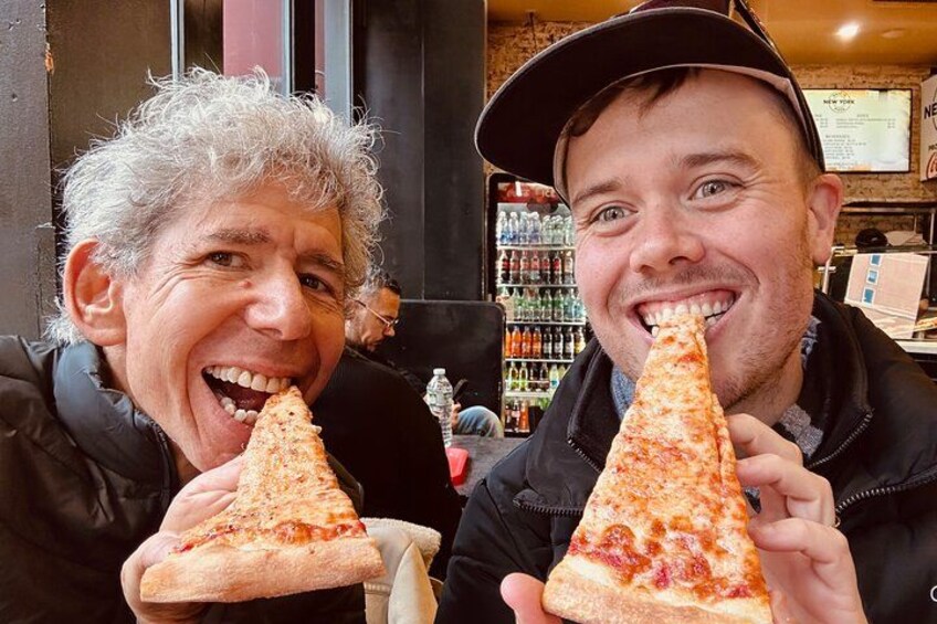 Two people holding triangular slices of pizza in a restaurant. 2