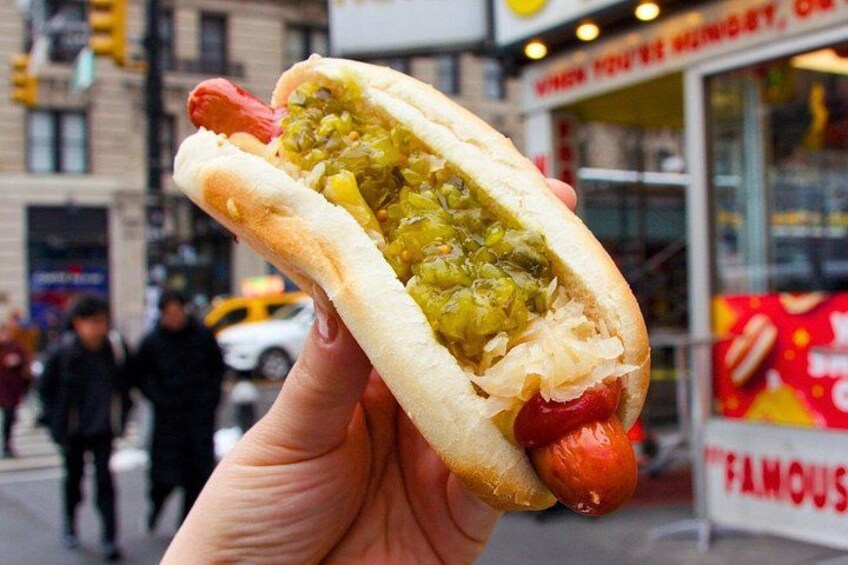 A hot dog with mustard and sauerkraut in a bun, held by a person. 1