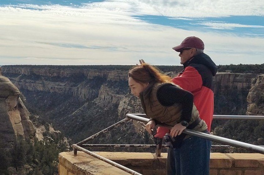 A person leaning on a railing overlooking a canyon with a vast landscape. 2