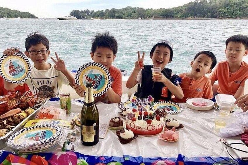 A group of people on a boat with a birthday cake and food. 1