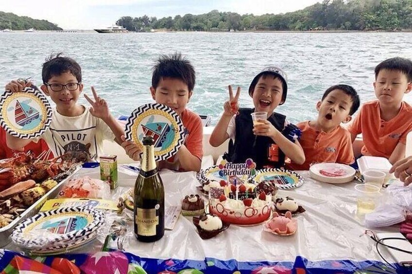 A group of people on a boat with a birthday cake and food. 1