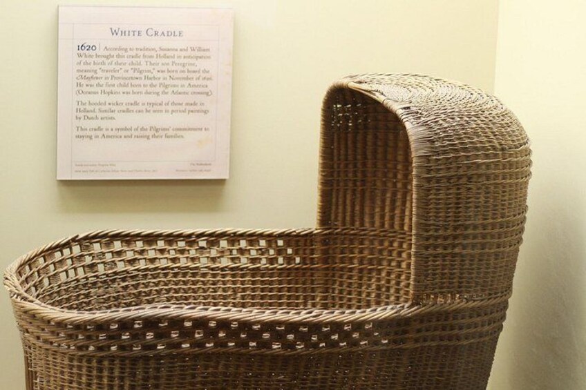 A wicker basket with a curved lid, displayed against a wall with a printed informational plaque. 1