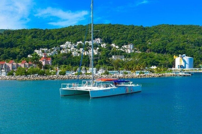 A sailboat docked at a marina with a backdrop of a hillside town and a clear blue sky. 2