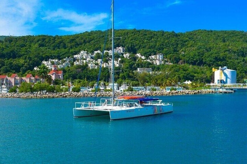 A sailboat docked at a harbor with a backdrop of a hillside town and a clear blue sky. 4
