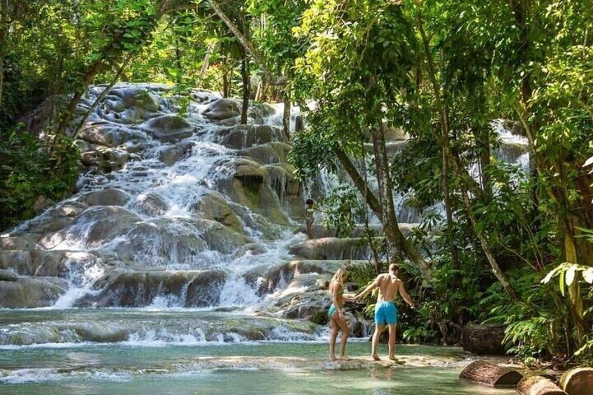 A waterfall in a forested area with two people standing in the water. 2