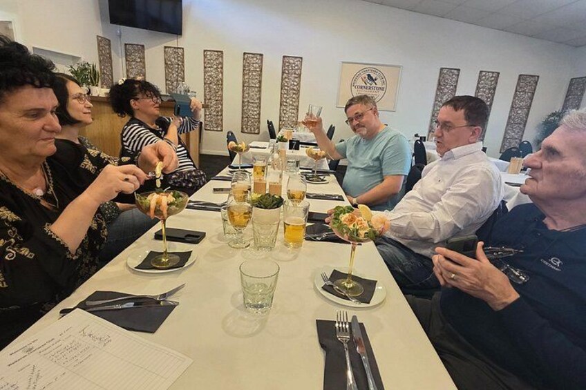 A group of people dining at a restaurant with a long table, glasses of beverages, and plates of food. 2