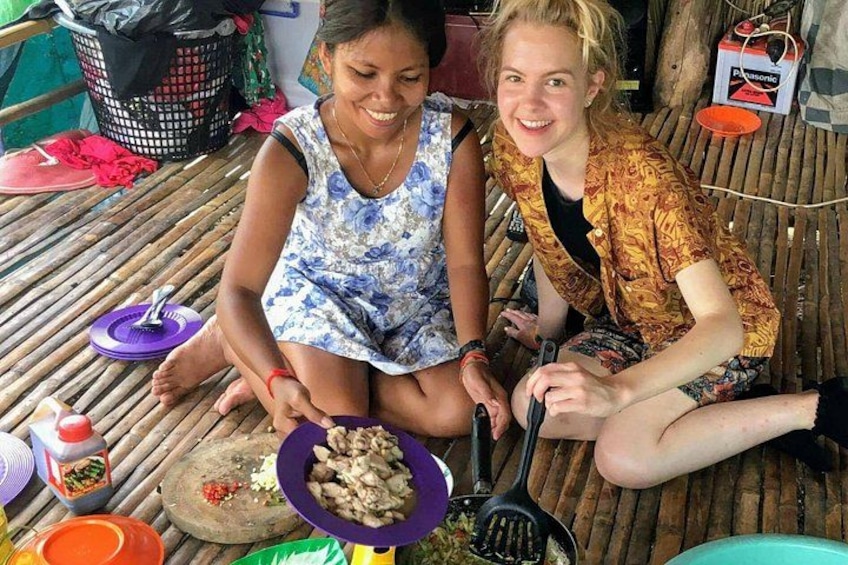 Two people sitting on a bamboo mat, one holding a plate of food and a spatula. 2