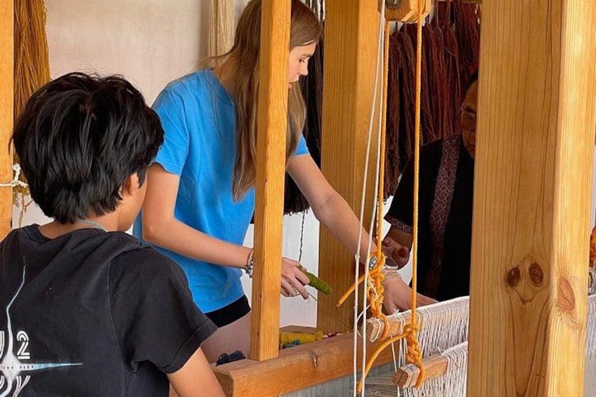 A person weaving on a loom with wooden structures and a child observing. 3