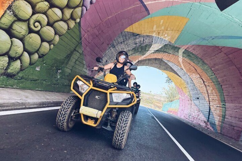 A person riding an ATV on a road with a colorful mural on the side. 5