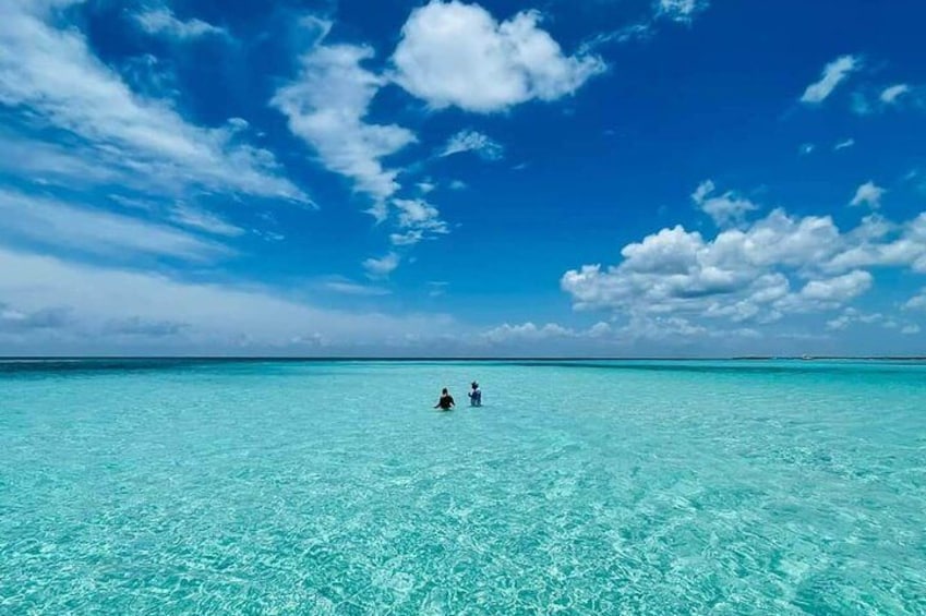 Una persona nadando en aguas turquesas cristalinas bajo un cielo azul con algunas nubes dispersas. 1