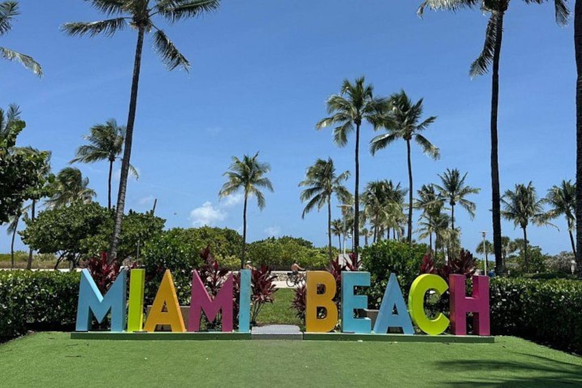 Colorful letters spelling 'MIAMI BEACH' on a grassy area with palm trees in the background. 2