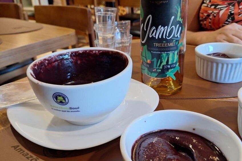 Et bord med en skål lilla mad, en flaske Jambu Treèmele og en lille hvid skål. 2