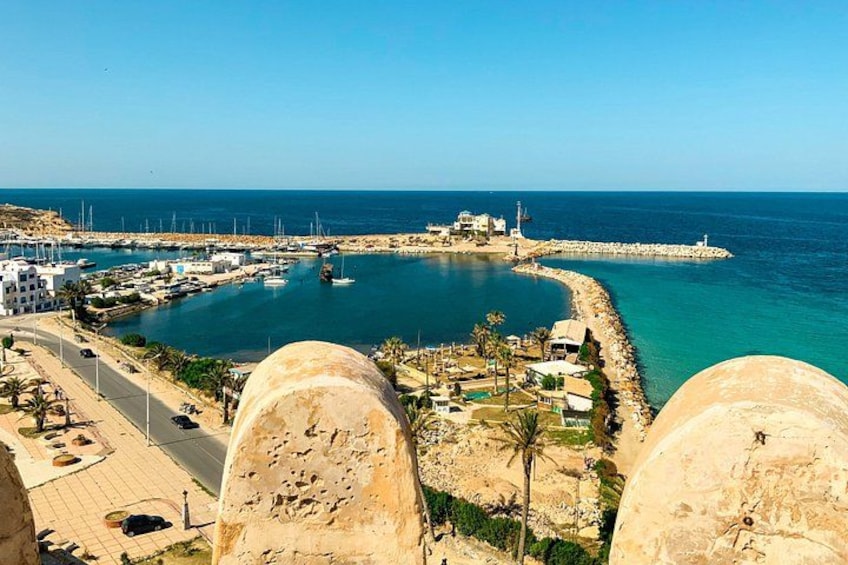 A coastal town with a marina, buildings, and a prominent rock formation. 1