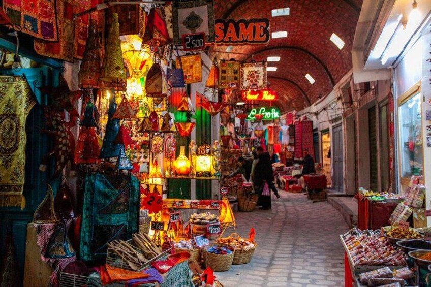 A bustling indoor market with various stalls selling colorful lanterns, textiles, and other goods. 3