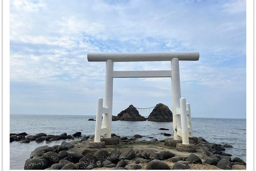 A white torii gate on a rocky shore with the ocean in the background. 1