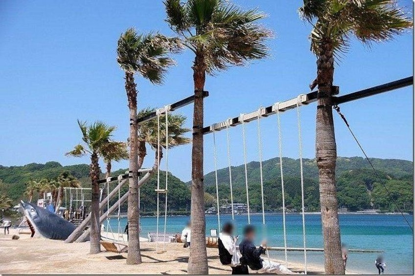 A beach with palm trees, a swing set, and a person sitting on the sand. 3