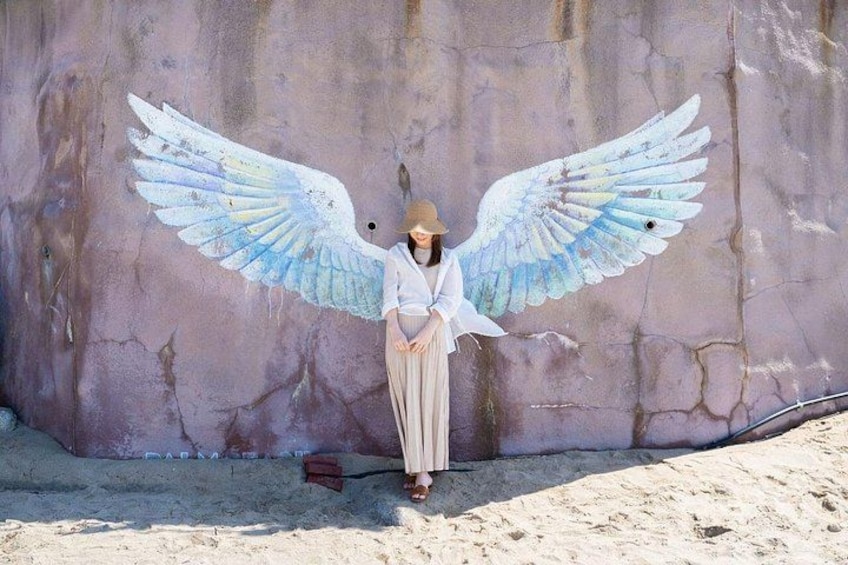 A person with large painted wings standing in front of a wall. 2