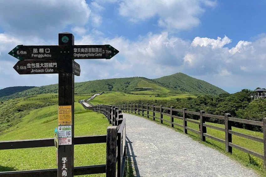 A viewpoint with a wooden fence, a signpost with directions, and a mountain landscape. 2