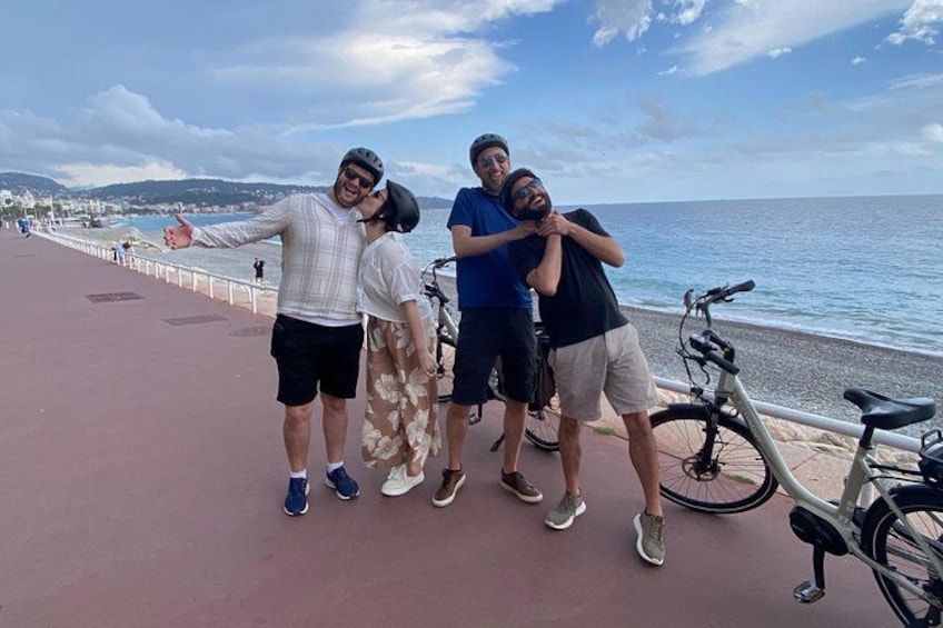 Three people posing by a seaside promenade with bicycles and a clear sky. 1
