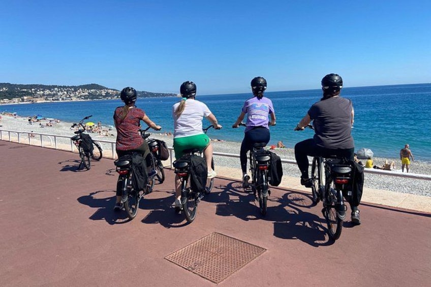 A group of people riding bicycles along a coastal promenade with the sea and beach in the background. 3