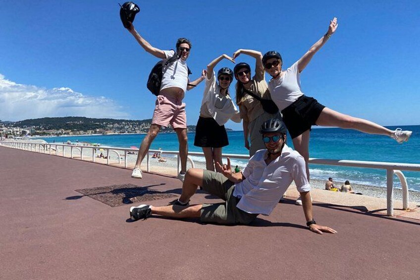 A group of people posing on a beach promenade with the sea and hills in the background. 5