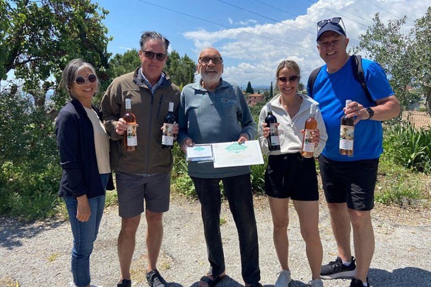 A group of people standing outdoors, holding bottles of wine and a certificate. 4